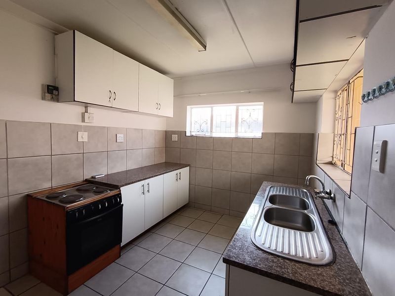 A functional kitchen featuring built-in cabinetry, laminate countertops, a double bowl stainless steel sink, and a freestanding electric stove with tiled finishes.