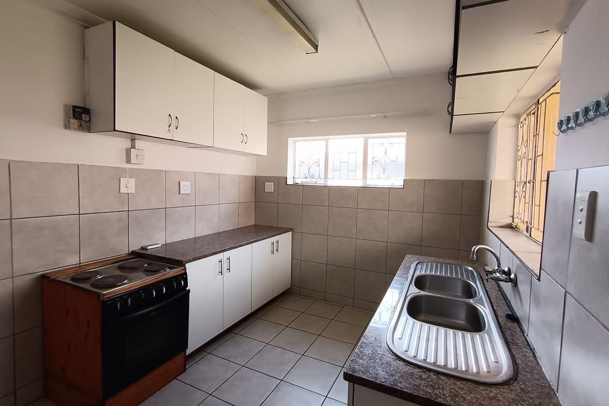 A functional kitchen featuring built-in cabinetry, laminate countertops, a double bowl stainless steel sink, and a freestanding electric stove with tiled finishes.