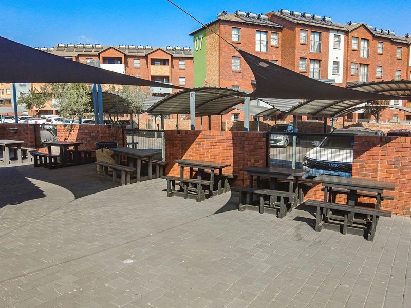 Outdoor communal entertainment area featuring paved flooring, brick boundary walls, and overhead shade sails within an apartment complex.