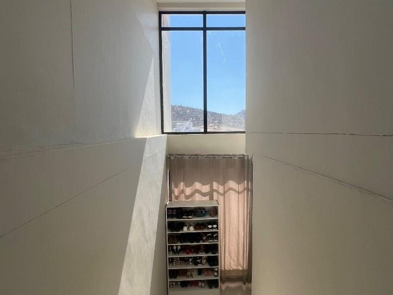 A bright, double-volume hallway featuring large fixed windows that allow for ample natural light and a clean, tiled floor finish.
