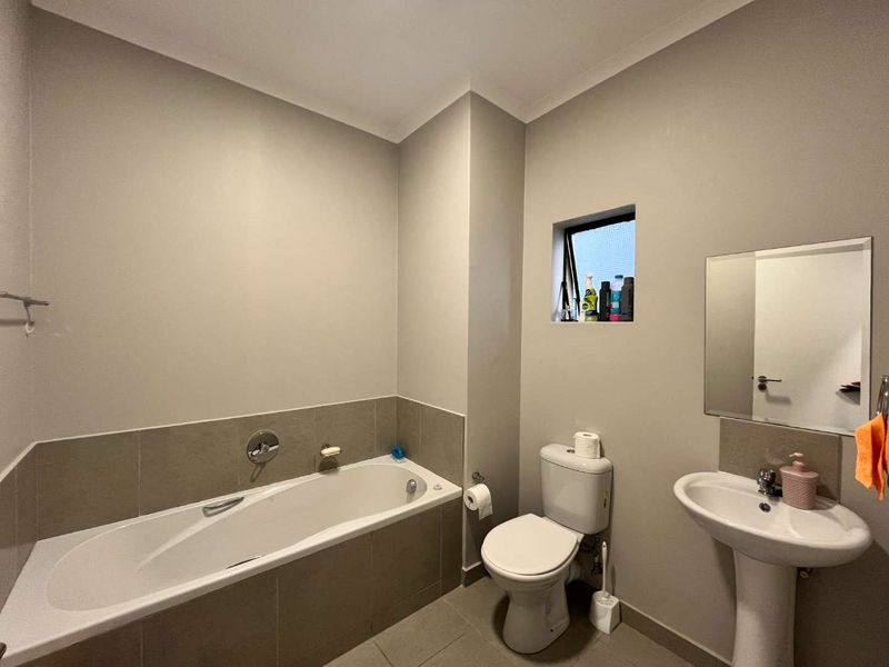 A functional bathroom featuring a bathtub, pedestal sink, and toilet with neutral wall finishes and tiled flooring.
