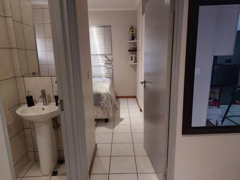 A bedroom featuring tiled flooring, built-in wall shelving, and an adjacent en-suite area with a pedestal basin.