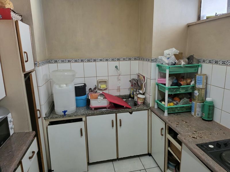 A compact kitchen featuring granite countertops, built-in cabinetry, and tiled splashbacks, offering a functional layout in need of cosmetic updates.