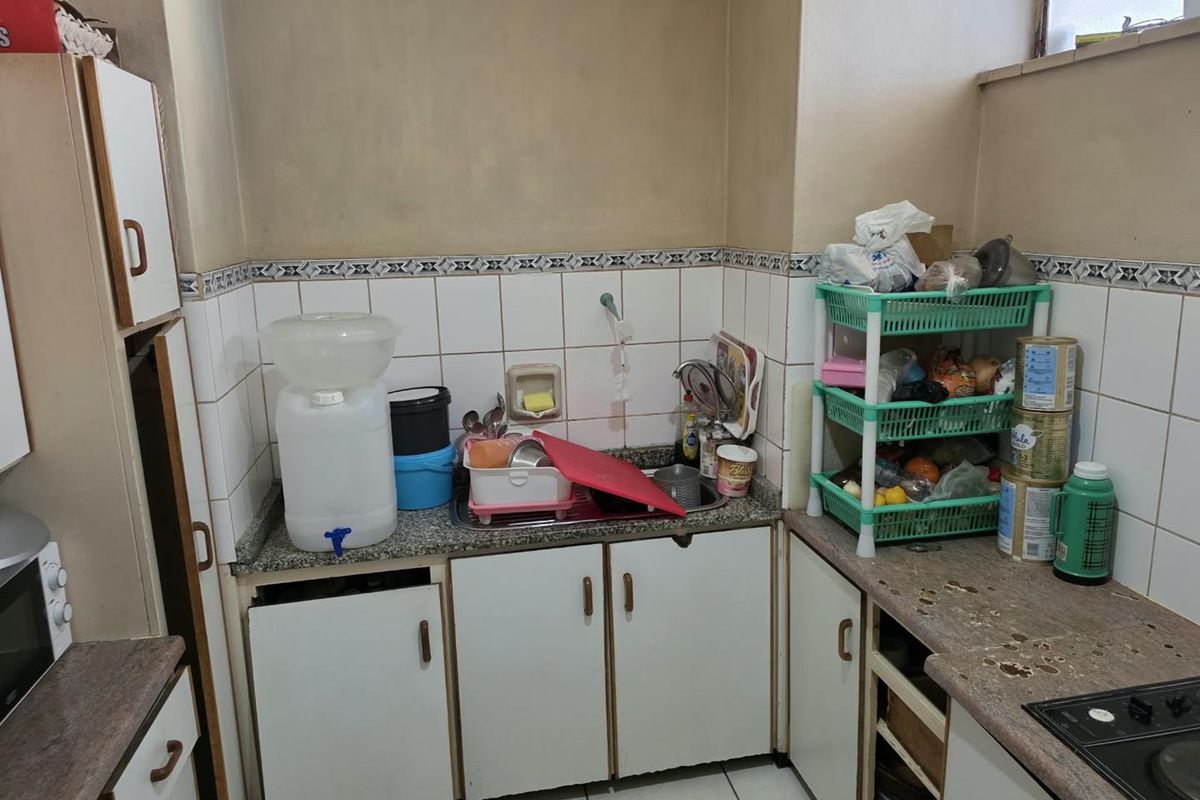 A compact kitchen featuring granite countertops, built-in cabinetry, and tiled splashbacks, offering a functional layout in need of cosmetic updates.
