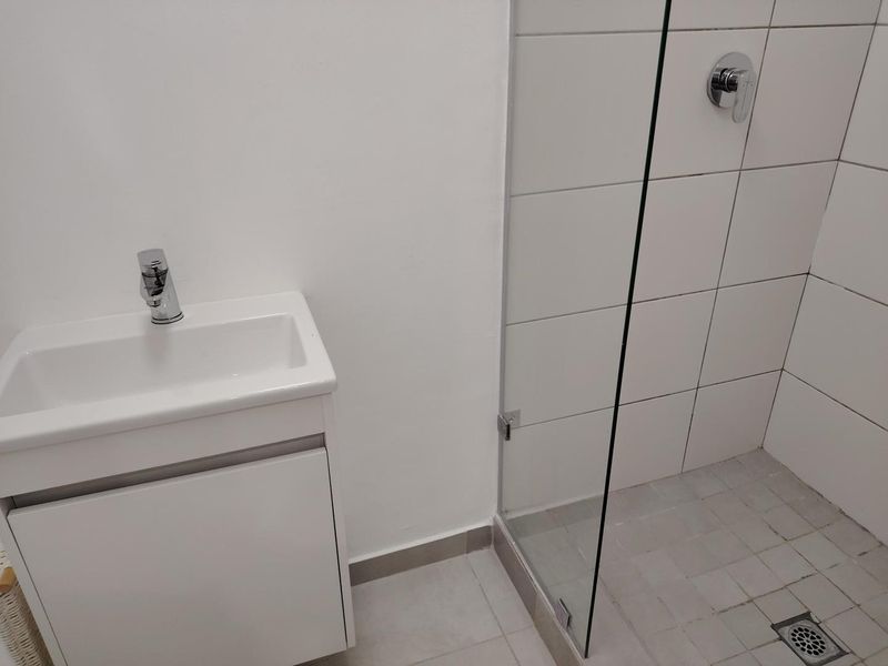 A clean, modern bathroom featuring a white vanity with basin and a glass-enclosed shower with tiled finishes.