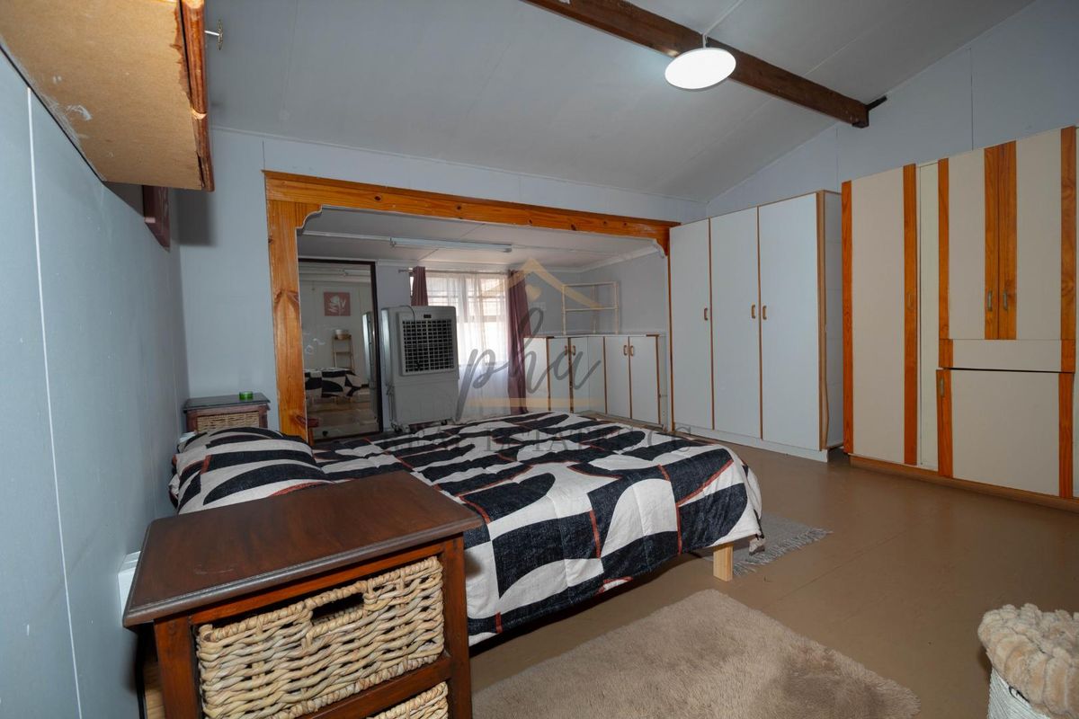 A spacious bedroom featuring built-in wooden wardrobes, exposed ceiling beams, and a neutral color palette, offering a functional layout with ample storage space.