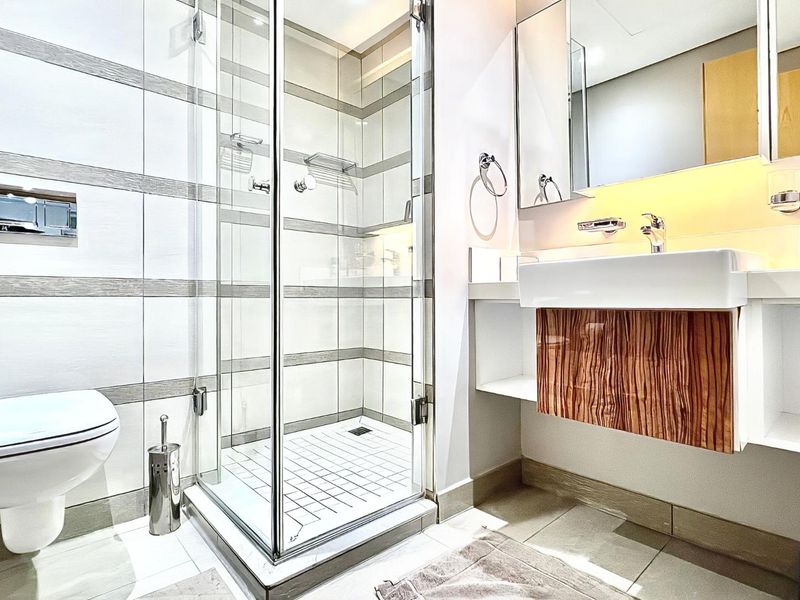 Modern bathroom featuring a glass shower enclosure, wall-mounted toilet, and a floating vanity with a basin and mirrored cabinet.