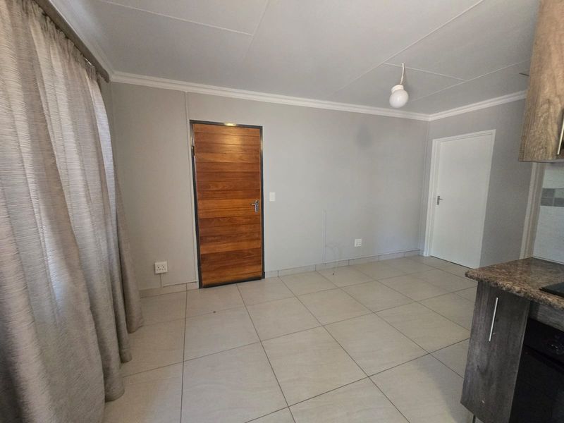 An open-plan living and kitchen area featuring neutral tiled flooring, modern cabinetry with granite countertops, and a feature wooden door.