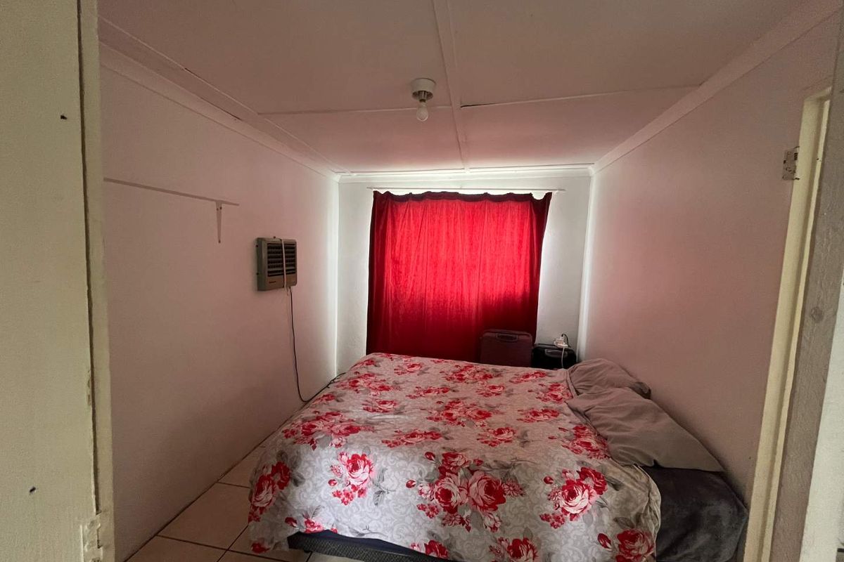 A compact bedroom featuring tiled flooring, a wall-mounted air conditioning unit, and a window covered by curtains.
