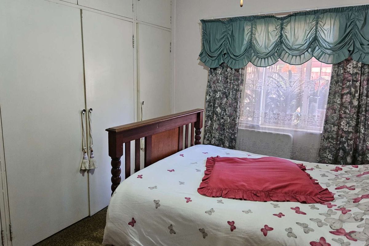 A bedroom featuring built-in cupboards and a window with traditional curtains, offering a functional and classic living space.