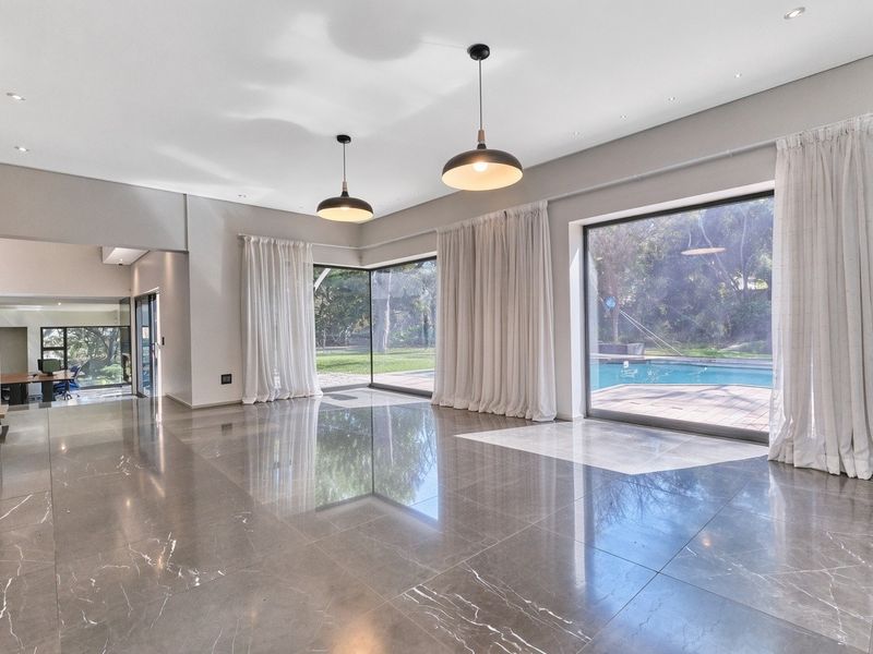 Spacious, light-filled living area featuring polished large-format floor tiles, modern pendant lighting, and expansive floor-to-ceiling glass doors opening to the pool area.