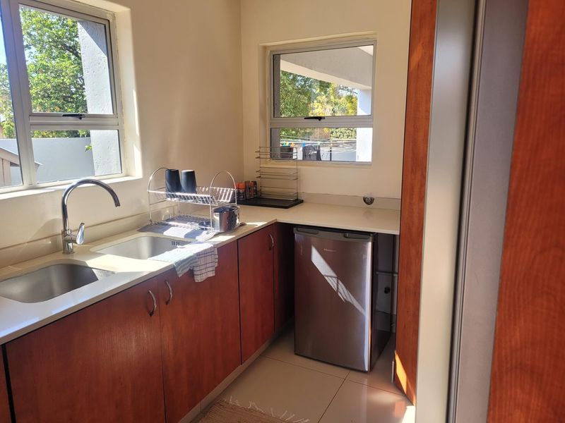 A functional scullery area featuring wood-finish cabinetry, stone countertops, a double sink with mixer tap, and tiled flooring.
