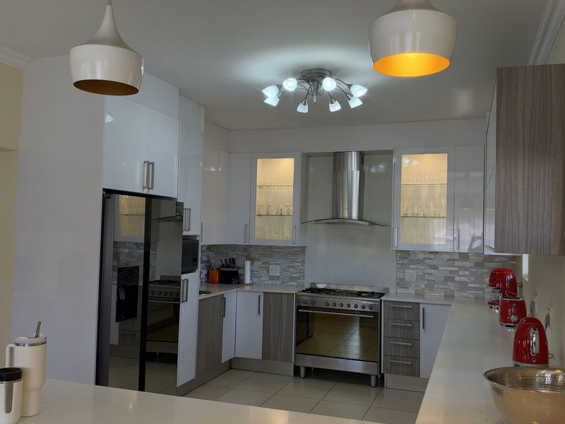 Modern kitchen featuring white and wood-tone cabinetry, stone countertops, a stainless steel gas stove with extractor fan, and stylish pendant lighting.