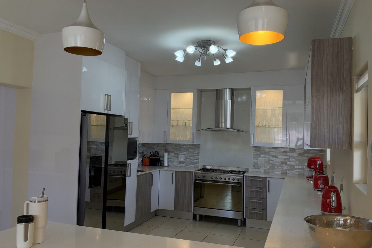 Modern kitchen featuring white and wood-tone cabinetry, stone countertops, a stainless steel gas stove with extractor fan, and stylish pendant lighting.