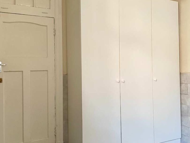 A bedroom featuring polished timber flooring, a classic panelled door with a transom window, and a large white built-in wardrobe.