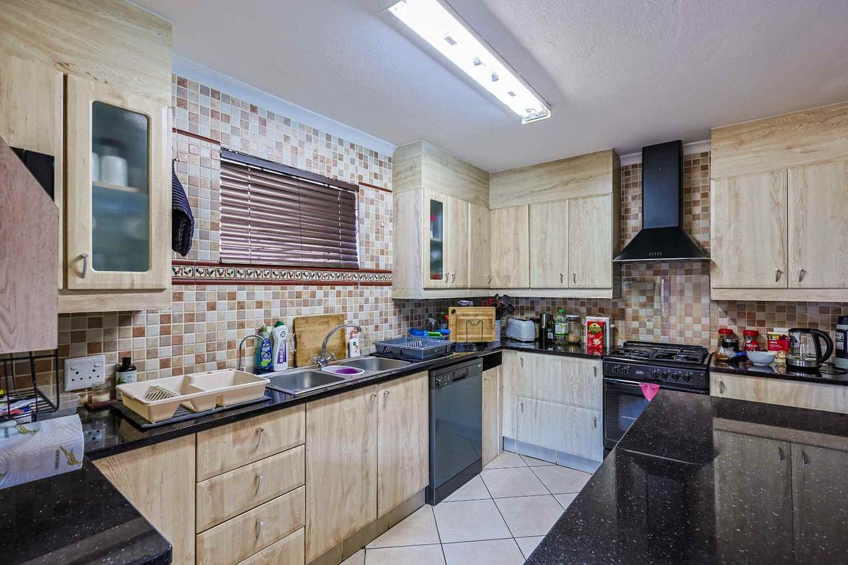 A functional kitchen featuring light wood-grain cabinetry, dark granite countertops, a built-in gas stove with extractor fan, and a double-basin sink.