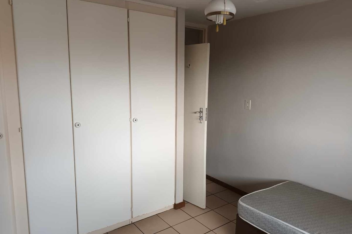 A bedroom featuring built-in cupboards, tiled flooring, and a ceiling fan, offering a functional space ready for personalization.