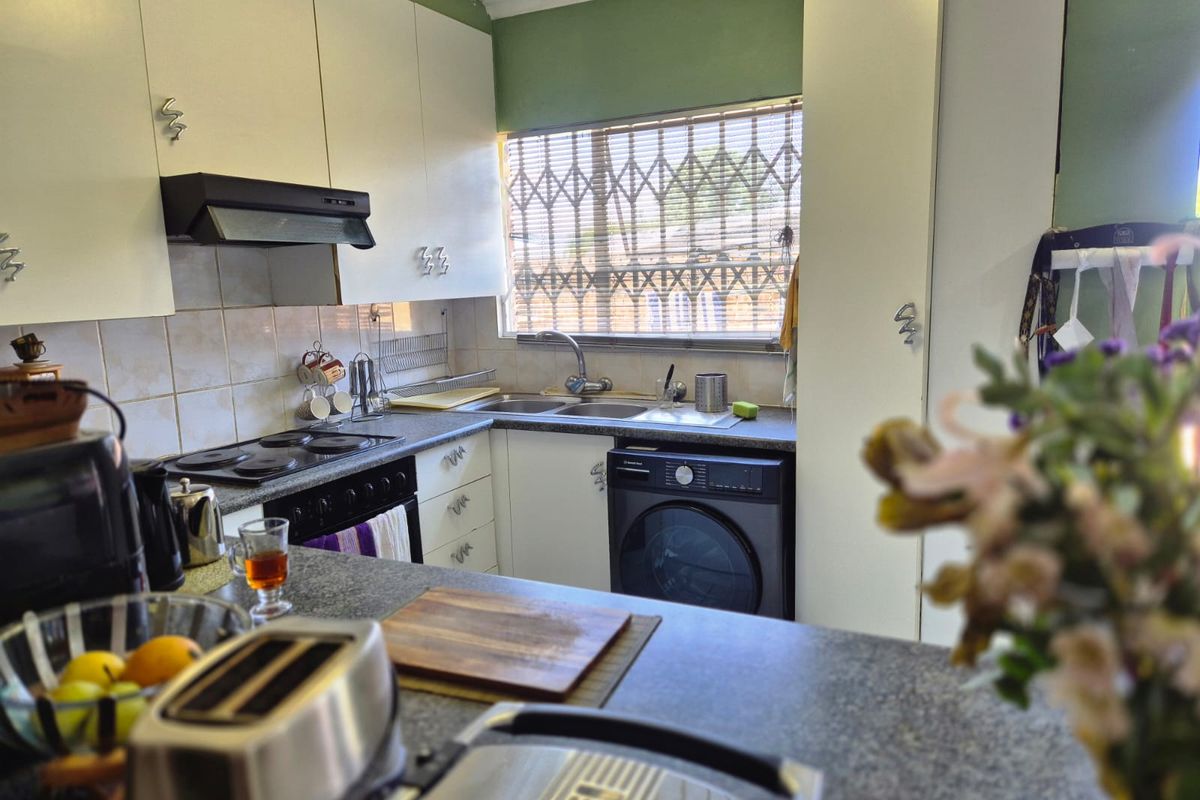 Functional kitchen featuring built-in cabinetry, electric hob with extractor fan, double sink, and tiled backsplash, offering a practical layout for daily meal preparation.