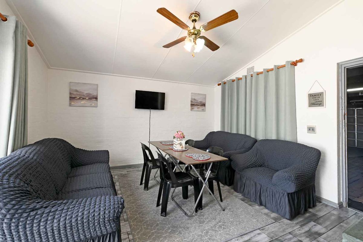 A functional living area featuring tiled flooring, painted brick walls, and a ceiling fan, providing a versatile space for relaxation and dining.