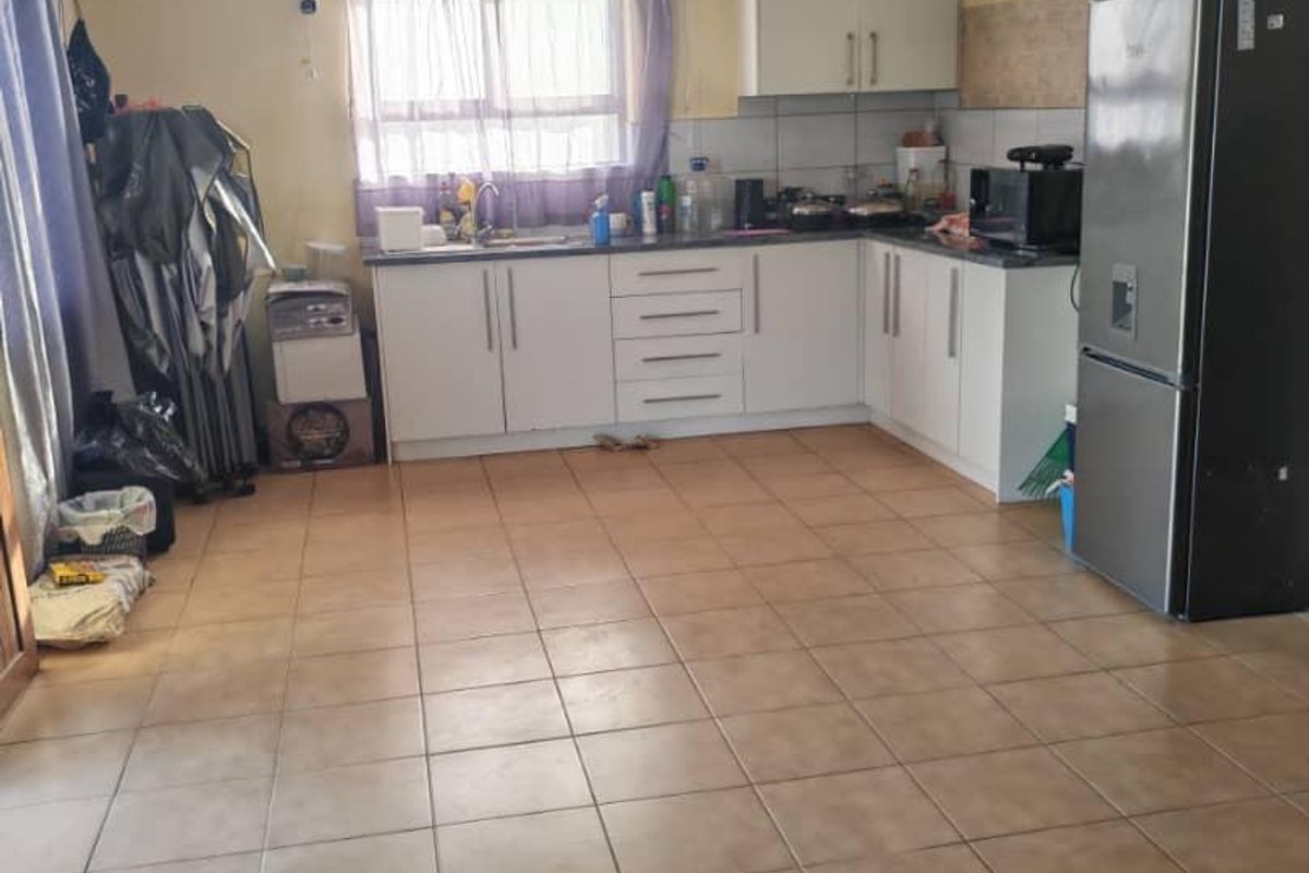 A functional kitchen featuring white built-in cabinetry, tiled flooring, and a stainless steel sink, offering a practical layout with potential for cosmetic updates.