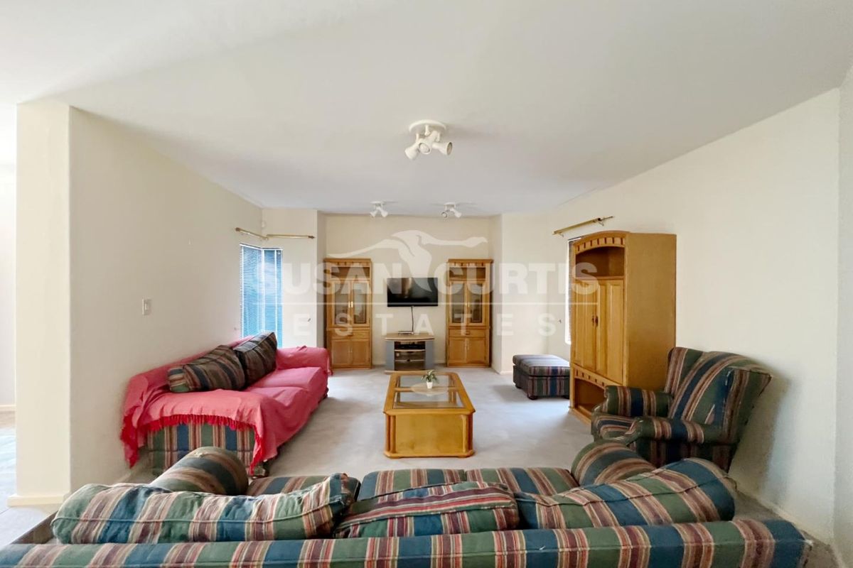 A spacious living room featuring neutral walls, carpeted flooring, and ceiling-mounted spotlights, offering a versatile layout for comfortable family living.