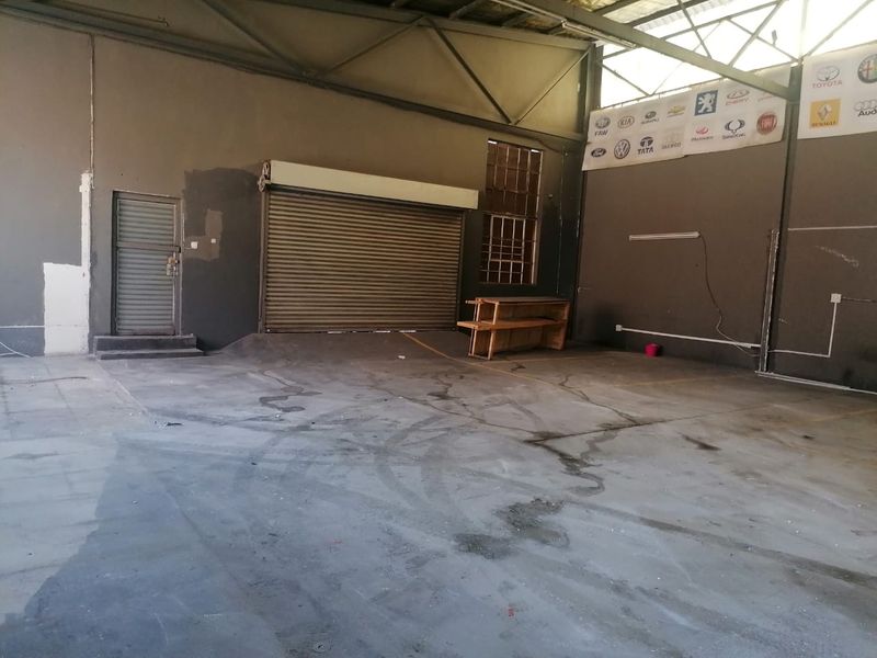Spacious industrial utility area featuring concrete flooring, exposed steel roof trusses, a large roller shutter door, and a secure steel entrance door.
