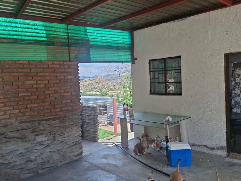 A covered outdoor patio area featuring exposed brick and stone masonry, concrete flooring, and a corrugated metal roof with views of the surrounding landscape.