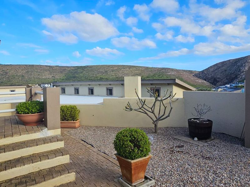 An elevated outdoor patio area featuring a built-in braai, paved flooring, and scenic mountain views, perfect for outdoor entertaining.