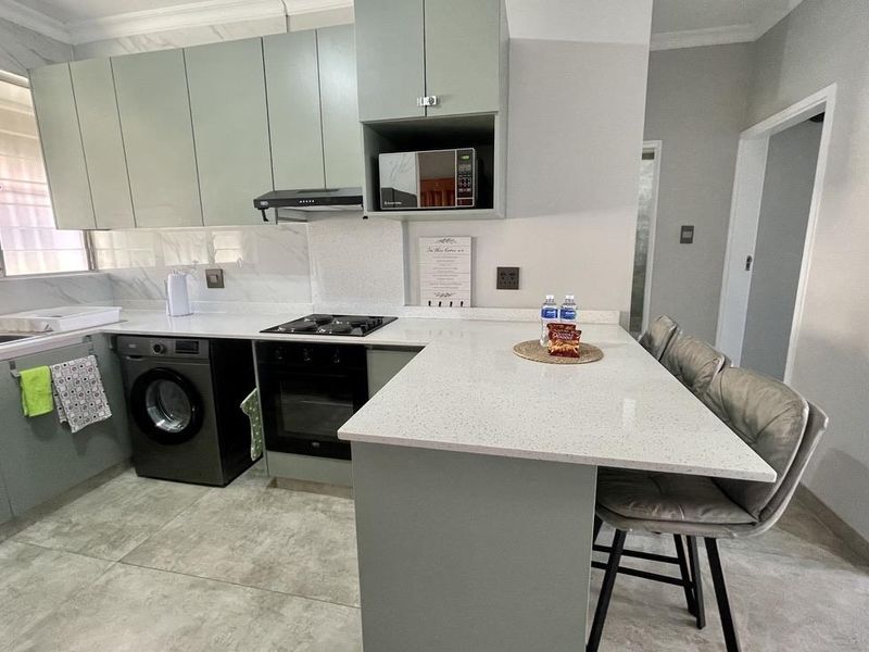 Modern kitchen featuring light green cabinetry, quartz countertops, integrated oven and hob, and a breakfast bar island with tiled flooring.
