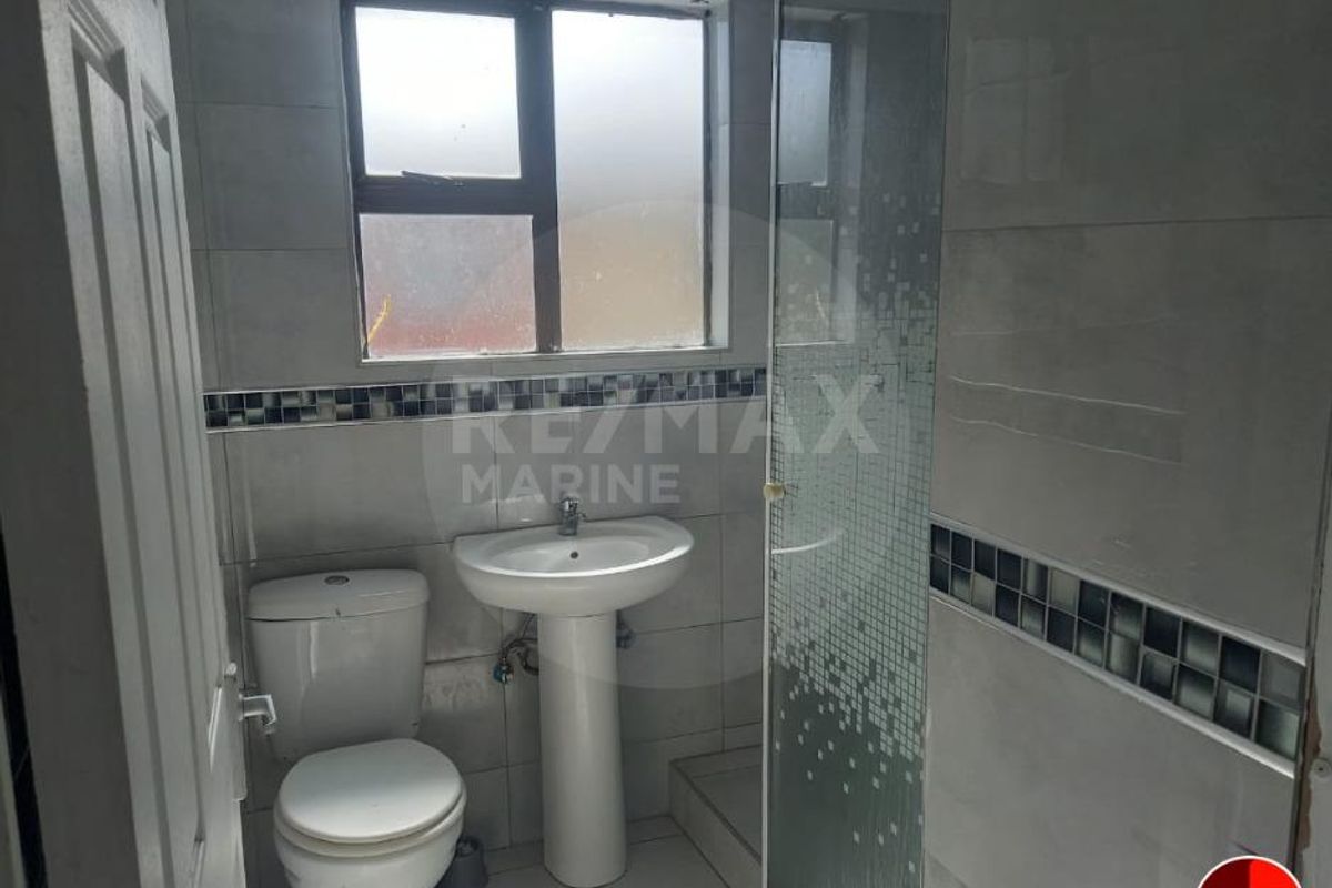 A compact bathroom featuring a pedestal basin, a toilet, and a glass-enclosed shower with tiled walls and decorative mosaic accents.