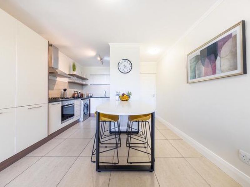 Modern open-plan kitchen featuring sleek cabinetry, integrated appliances, and a central island with seating, finished with neutral tiled flooring throughout.