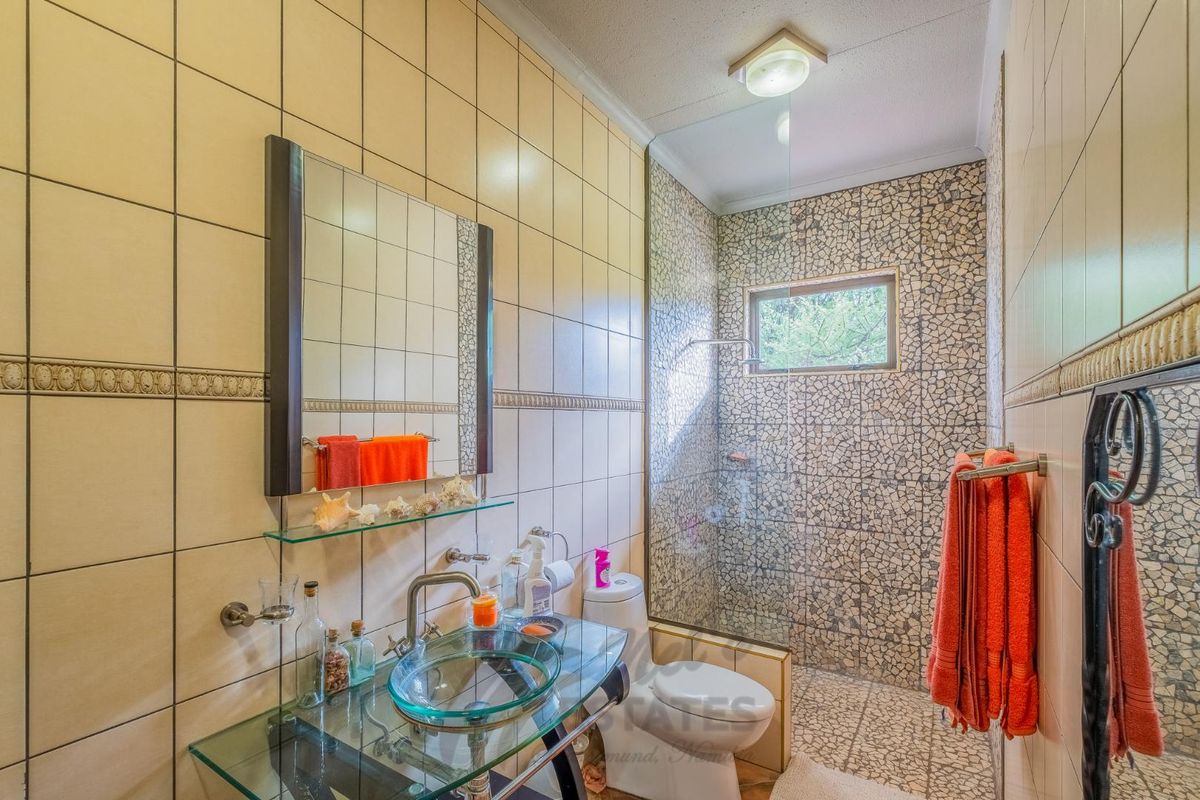 A functional bathroom featuring a glass vessel sink, wall-mounted mirror, and a walk-in shower with decorative stone-style wall tiling.