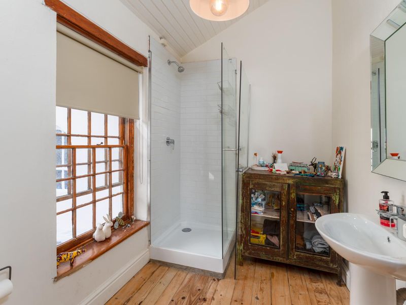 A bright bathroom featuring a glass-enclosed shower with subway tiling, a pedestal sink, and original timber flooring under a vaulted tongue and groove ceiling.
