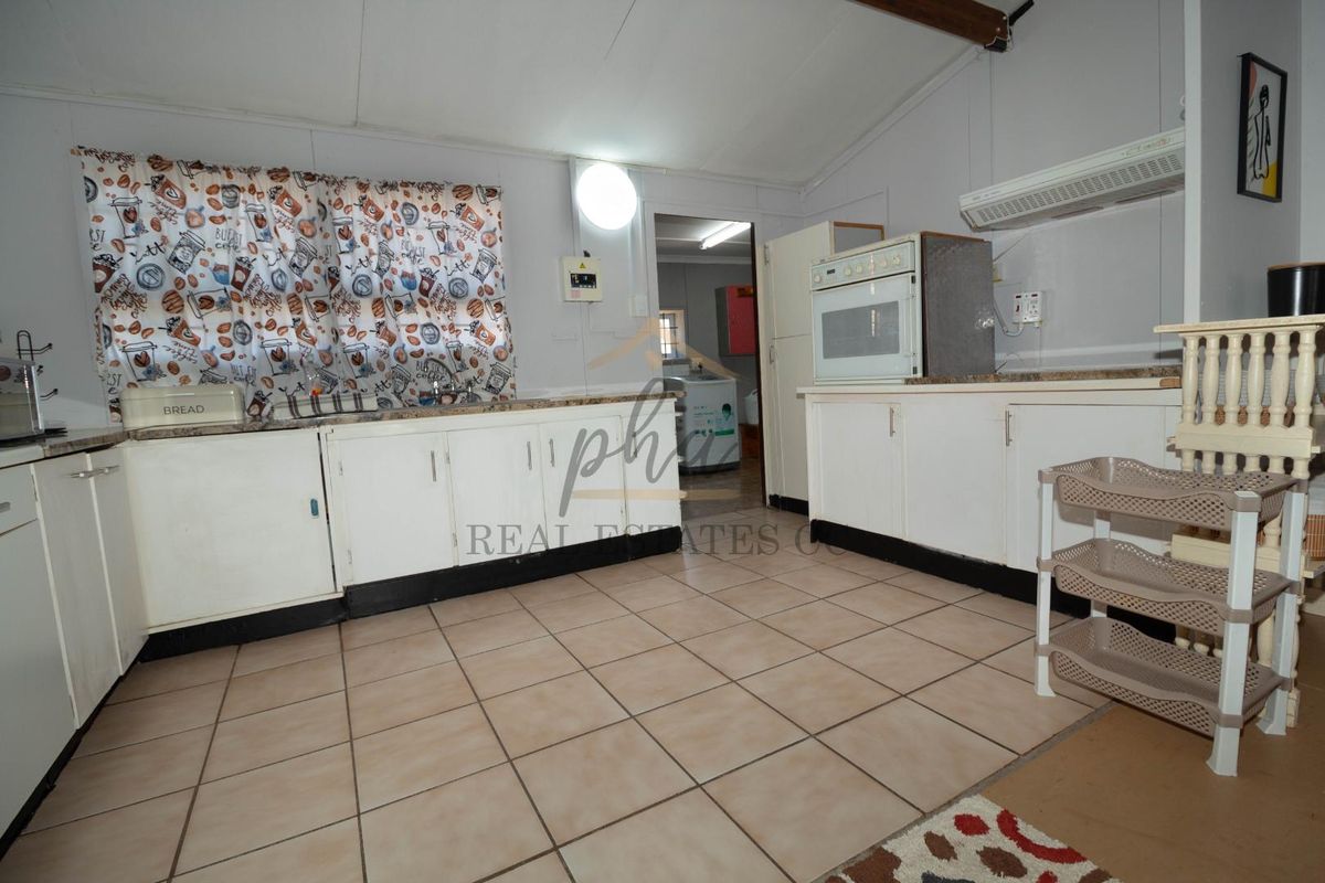 A functional kitchen featuring tiled flooring, laminate countertops, built-in cabinetry, and an integrated oven with an extractor fan.