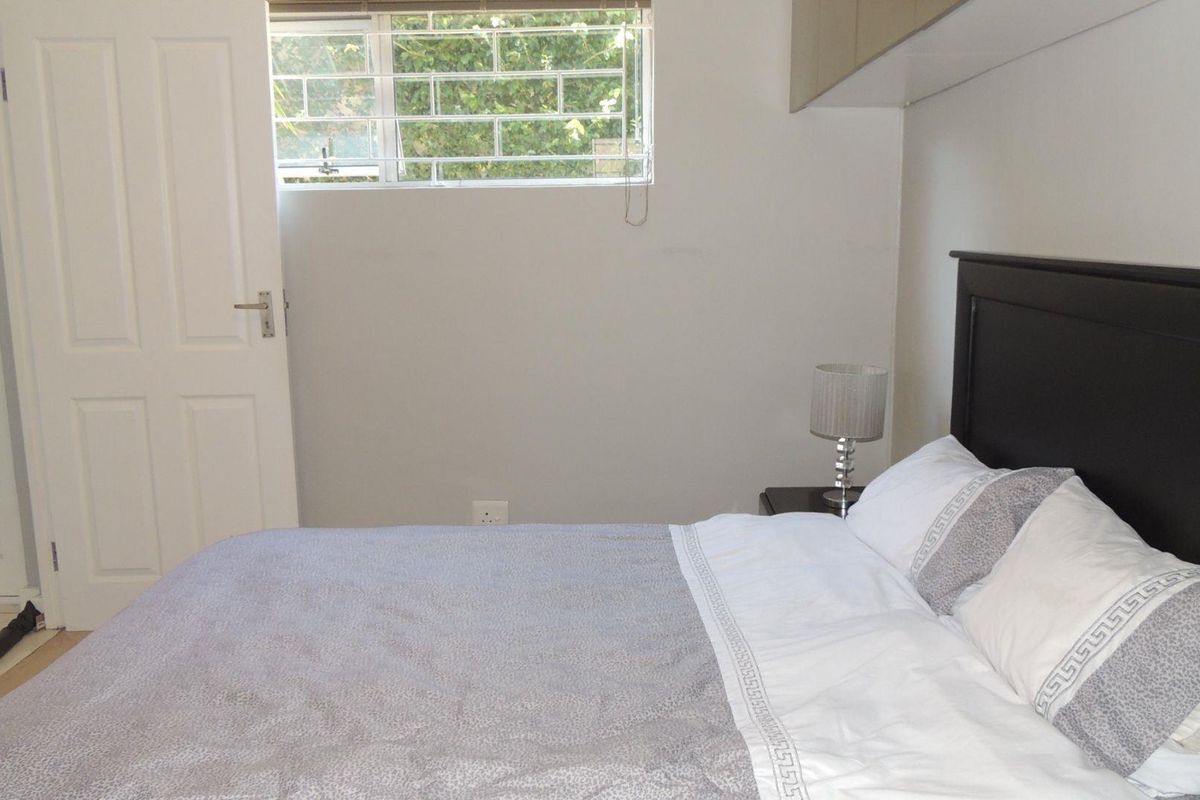 A functional bedroom featuring built-in cupboards and a window with security bars, providing a practical and secure living space.