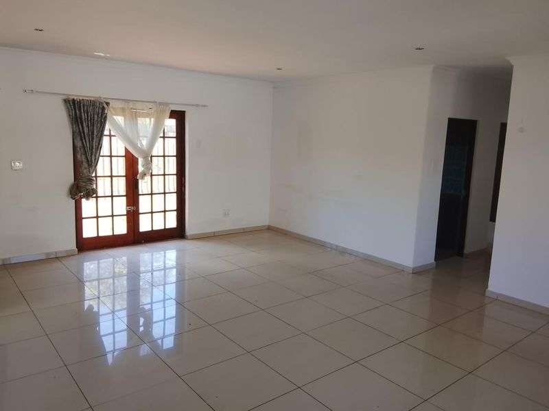 Spacious, light-filled living area featuring neutral tiled flooring, recessed downlighting, and wooden french doors providing access to the exterior.