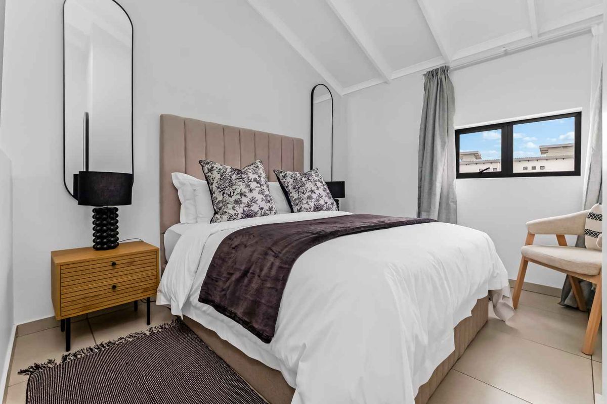 A bright and modern bedroom featuring vaulted ceilings, tiled flooring, and a window providing natural light.