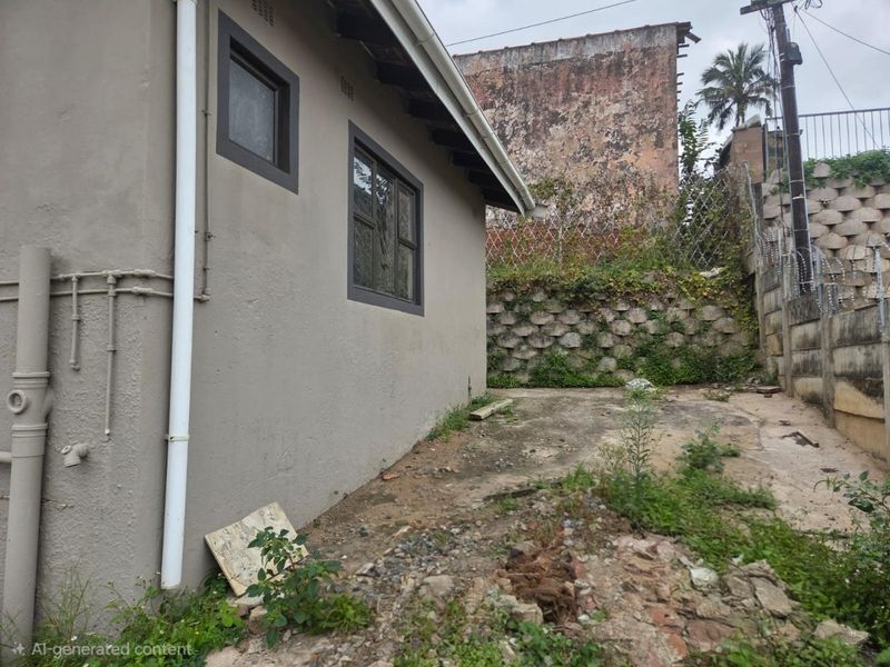 Rear exterior view of the property showing a concrete area, retaining wall, and security fencing, requiring maintenance and landscaping.