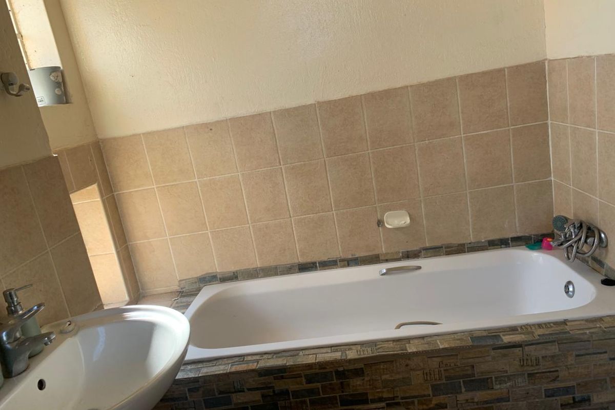 A functional bathroom featuring a built-in bathtub with decorative mosaic tiling and a pedestal basin with chrome fixtures.