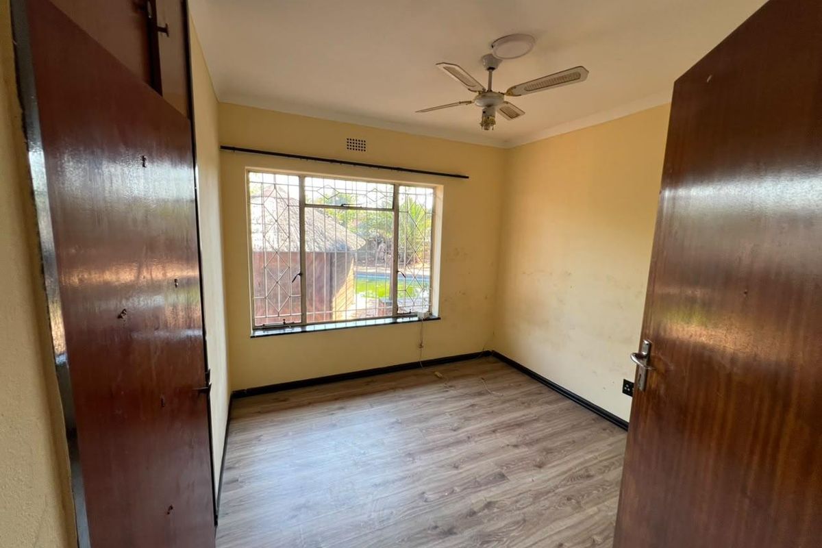 An empty bedroom featuring laminate flooring, a ceiling fan, and built-in cupboards, with security bars installed on the window.