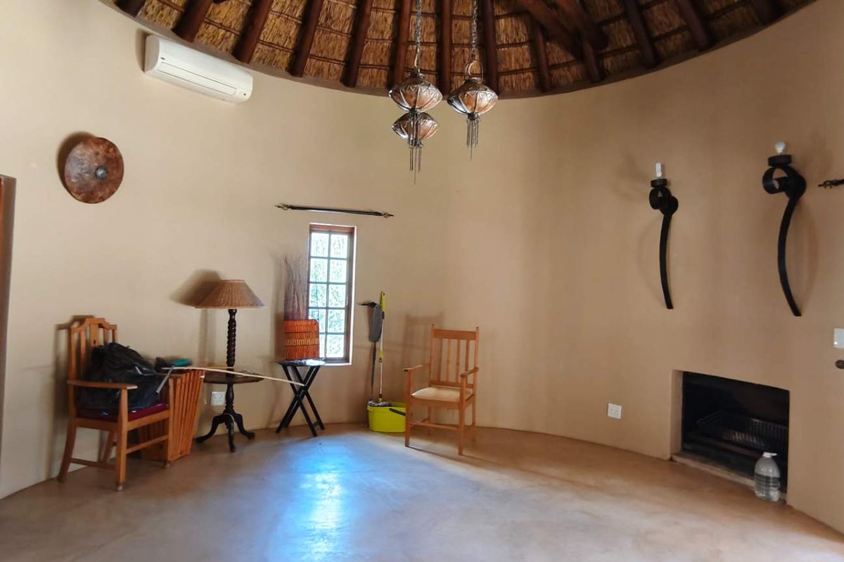 A circular living room featuring a traditional thatched roof, built-in fireplace, and polished concrete flooring, offering a unique architectural aesthetic.