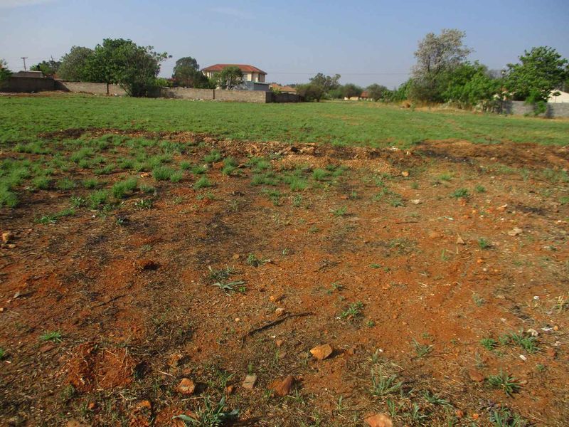 A view of a vacant residential plot featuring open grass, natural soil, and a perimeter boundary wall in a suburban setting.