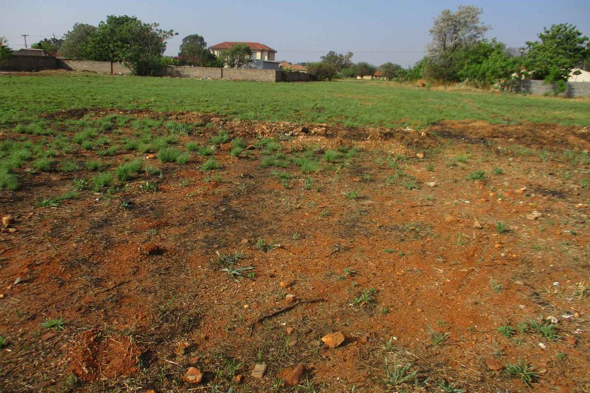 A view of a vacant residential plot featuring open grass, natural soil, and a perimeter boundary wall in a suburban setting.