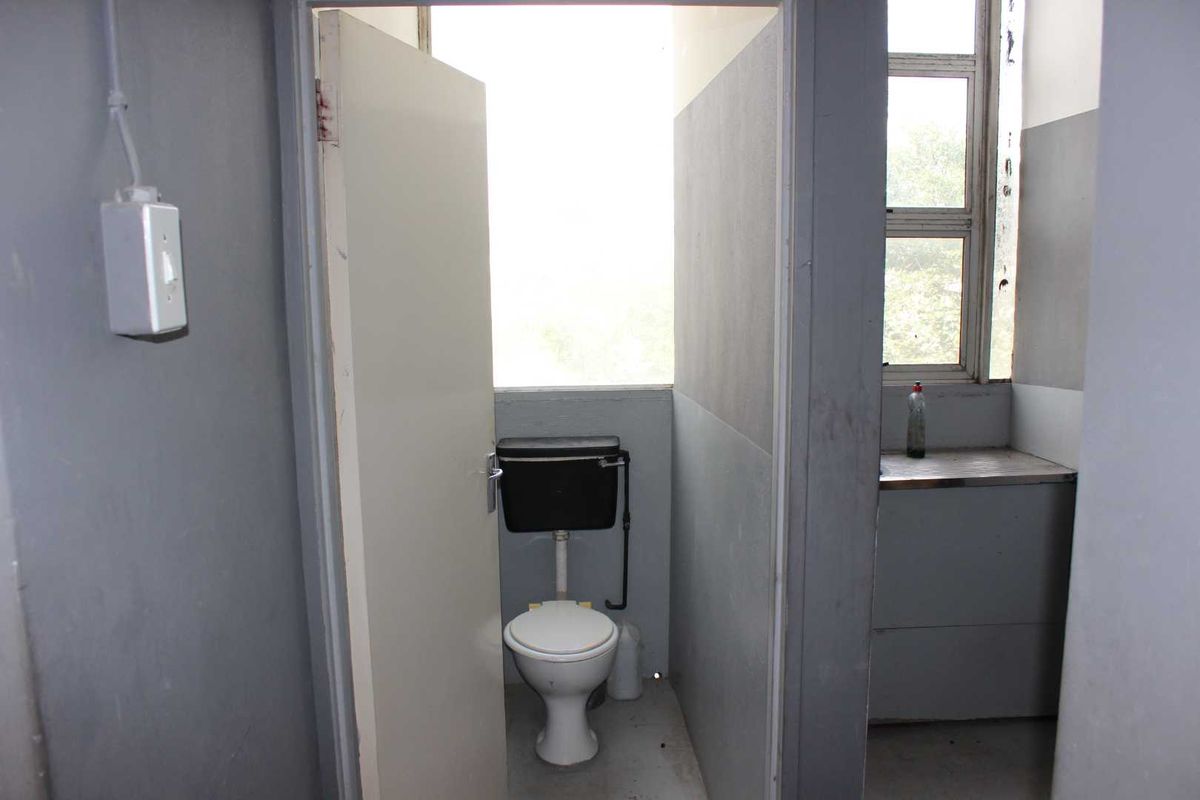 A functional industrial-style restroom facility featuring a standard toilet and a small adjacent wash area with a metal counter.