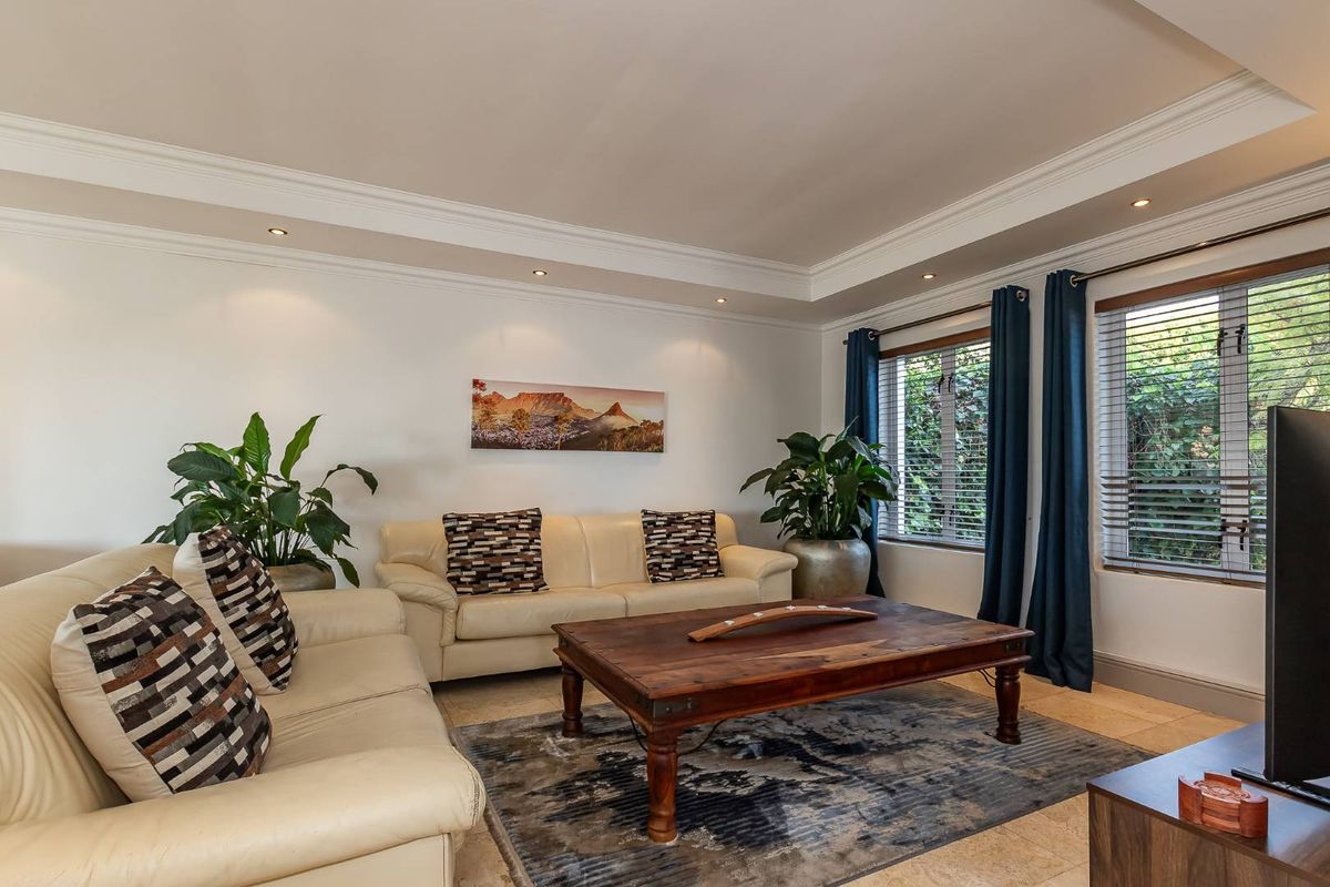 A well-maintained living room featuring tiled flooring, recessed downlighting, crown molding, and large windows with fitted venetian blinds.