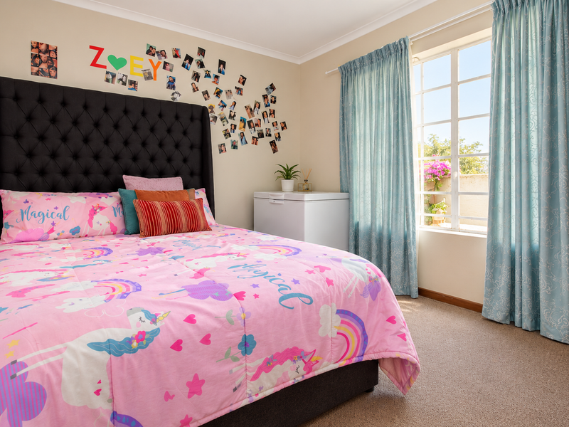 A well-lit bedroom featuring neutral walls, carpeted flooring, and a large window with curtains, providing a comfortable and functional living space.