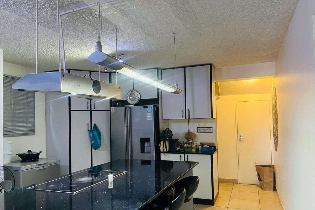 A functional kitchen featuring a central island with a built-in electric cooktop, overhead extractor fan, and ample cabinetry with a modern black and white finish.