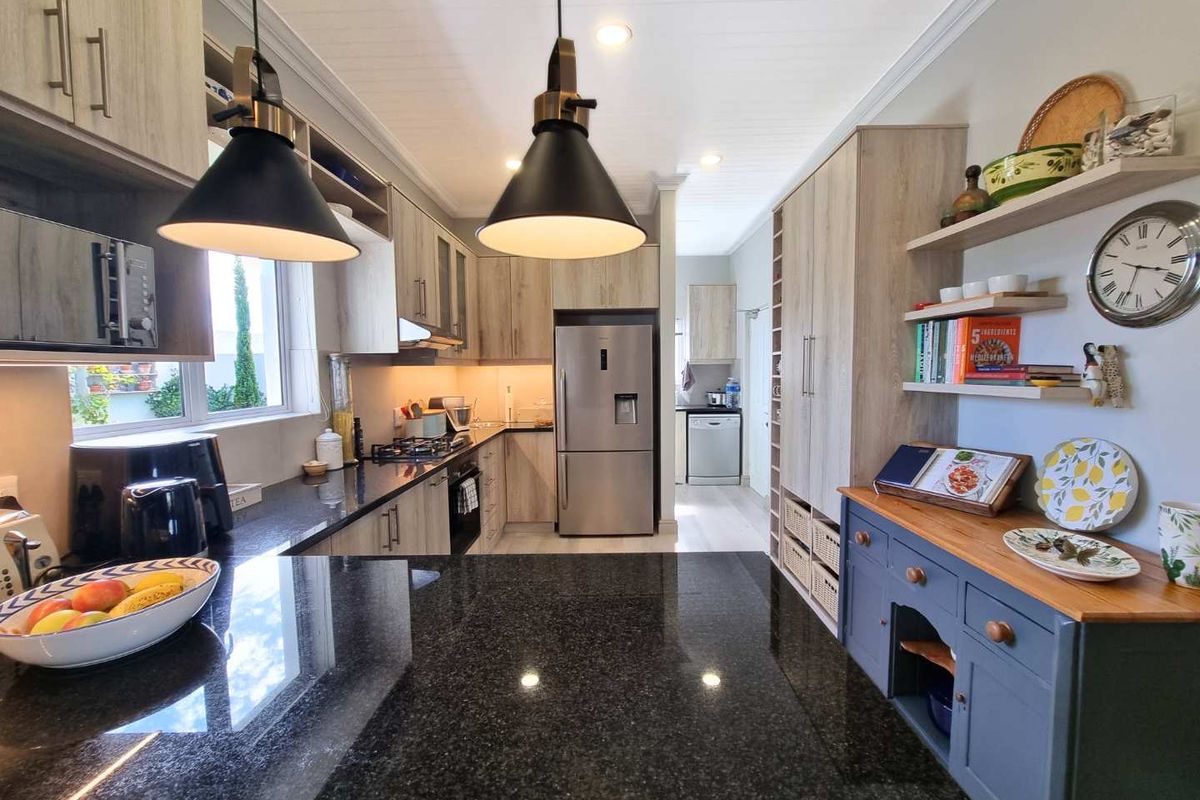 Modern kitchen featuring granite countertops, light wood cabinetry, integrated appliances, and stylish pendant lighting, with an open-plan layout leading to a scullery area.