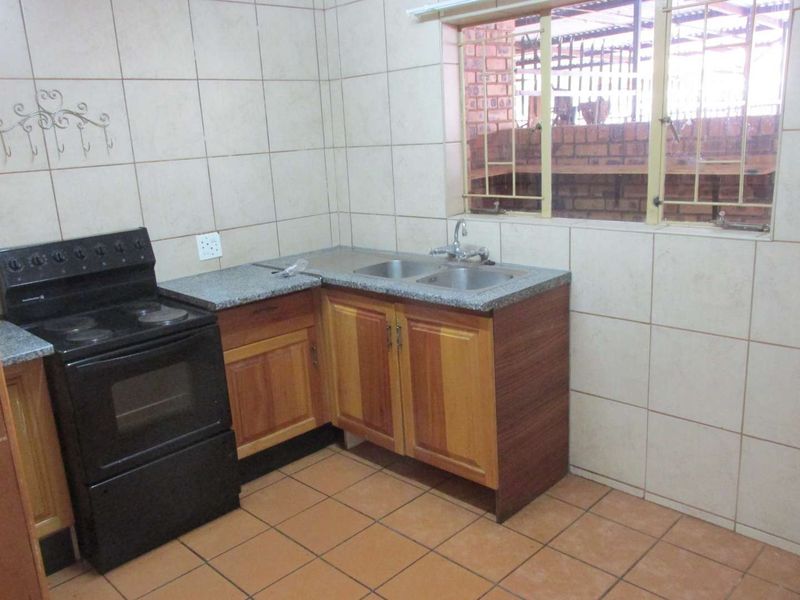 A functional kitchen featuring tiled walls and flooring, wooden cabinetry, granite countertops, and a double sink with a window view.