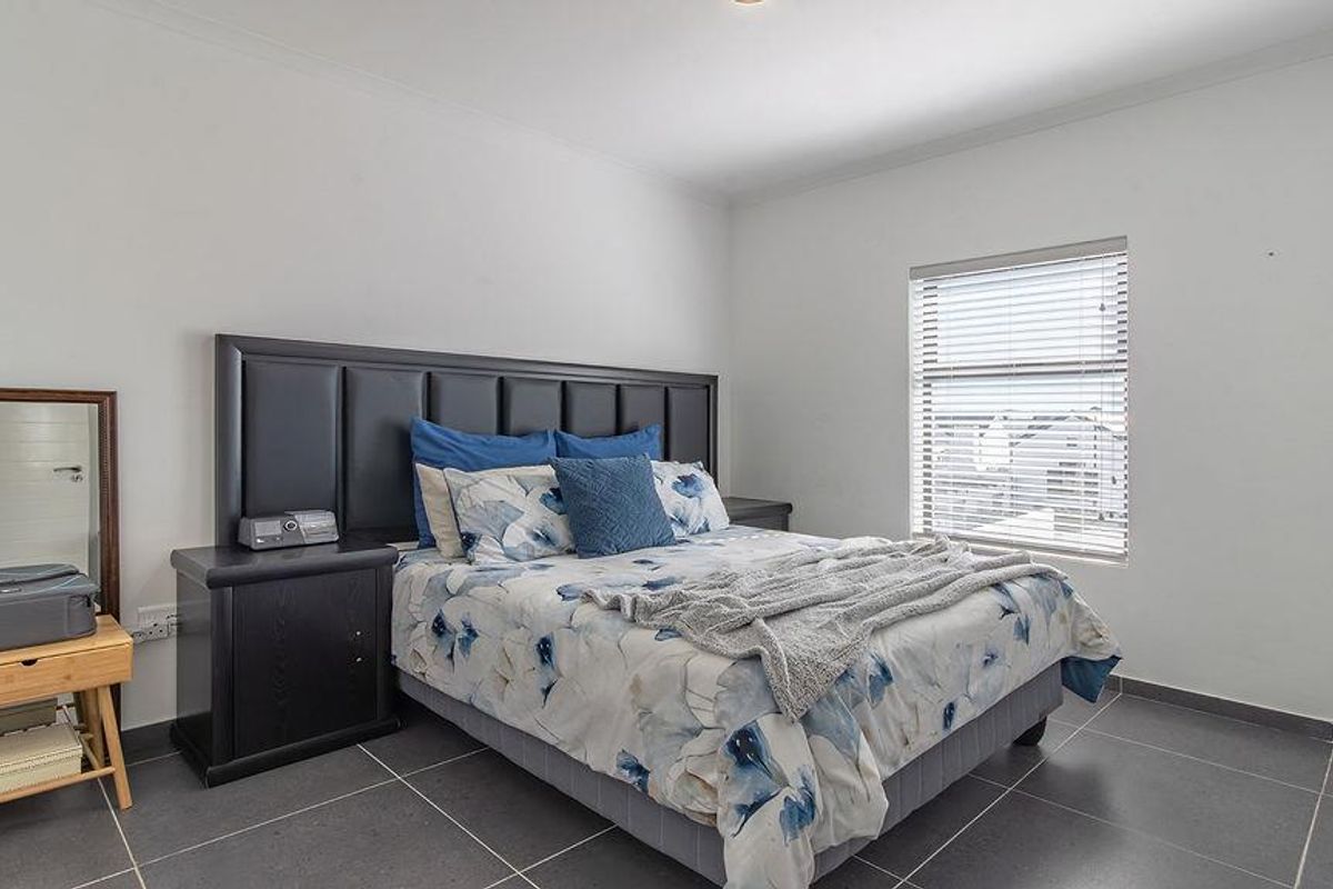 A well-lit bedroom featuring large format floor tiles, a window with fitted blinds, and neutral wall finishes.
